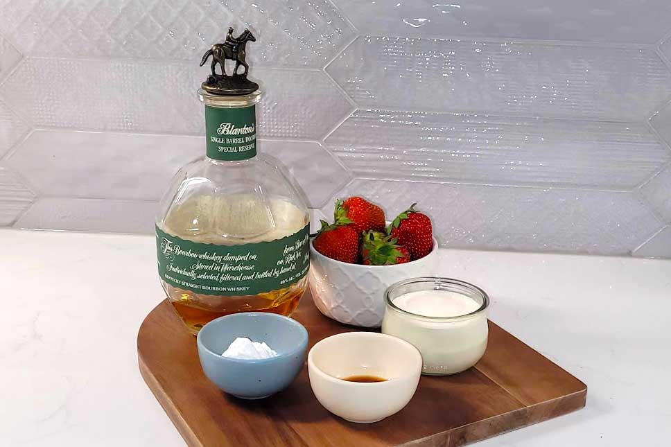 Bourbon, strawberries, whipping cream, sugar and vanilla on a counter.