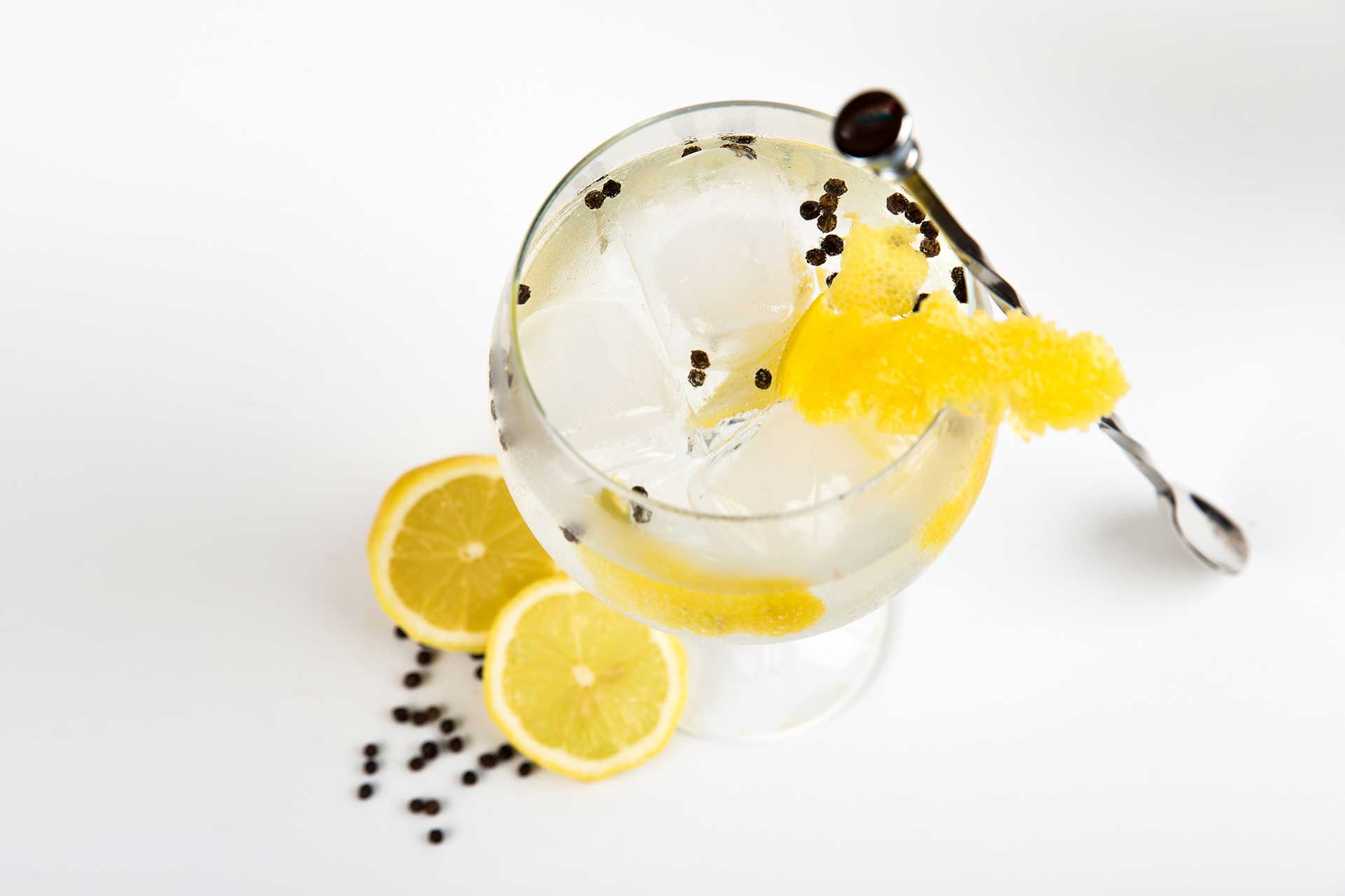 Glass filled with gin with peppercorns and lemon.