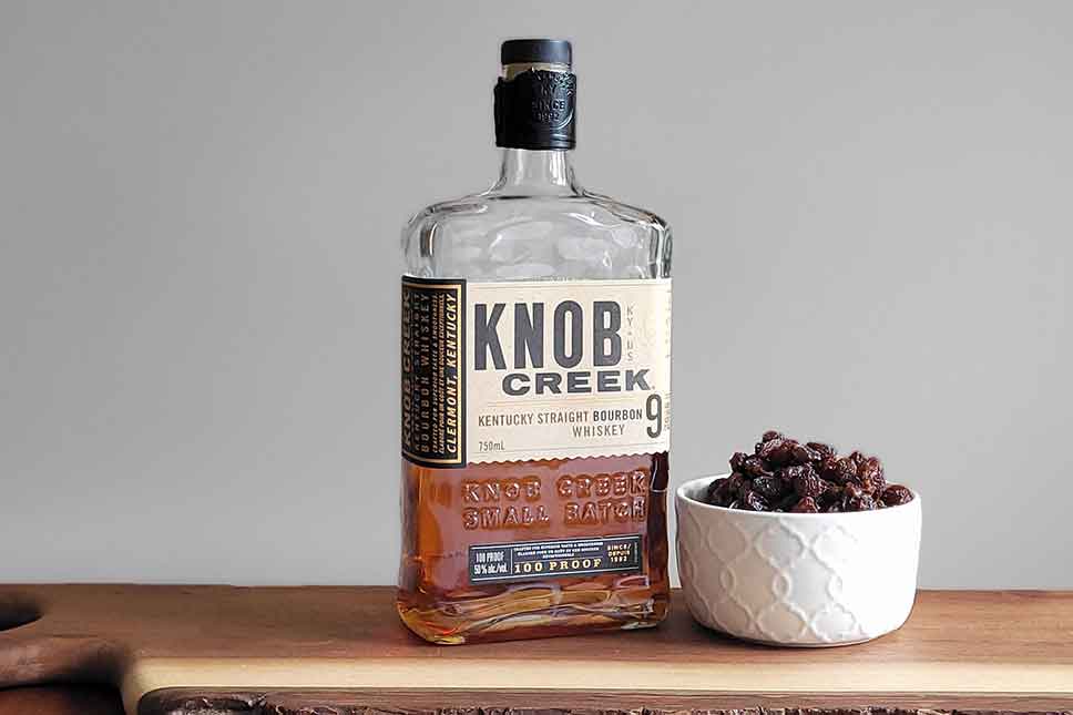 Raisins and a bottle of bourbon on a table.