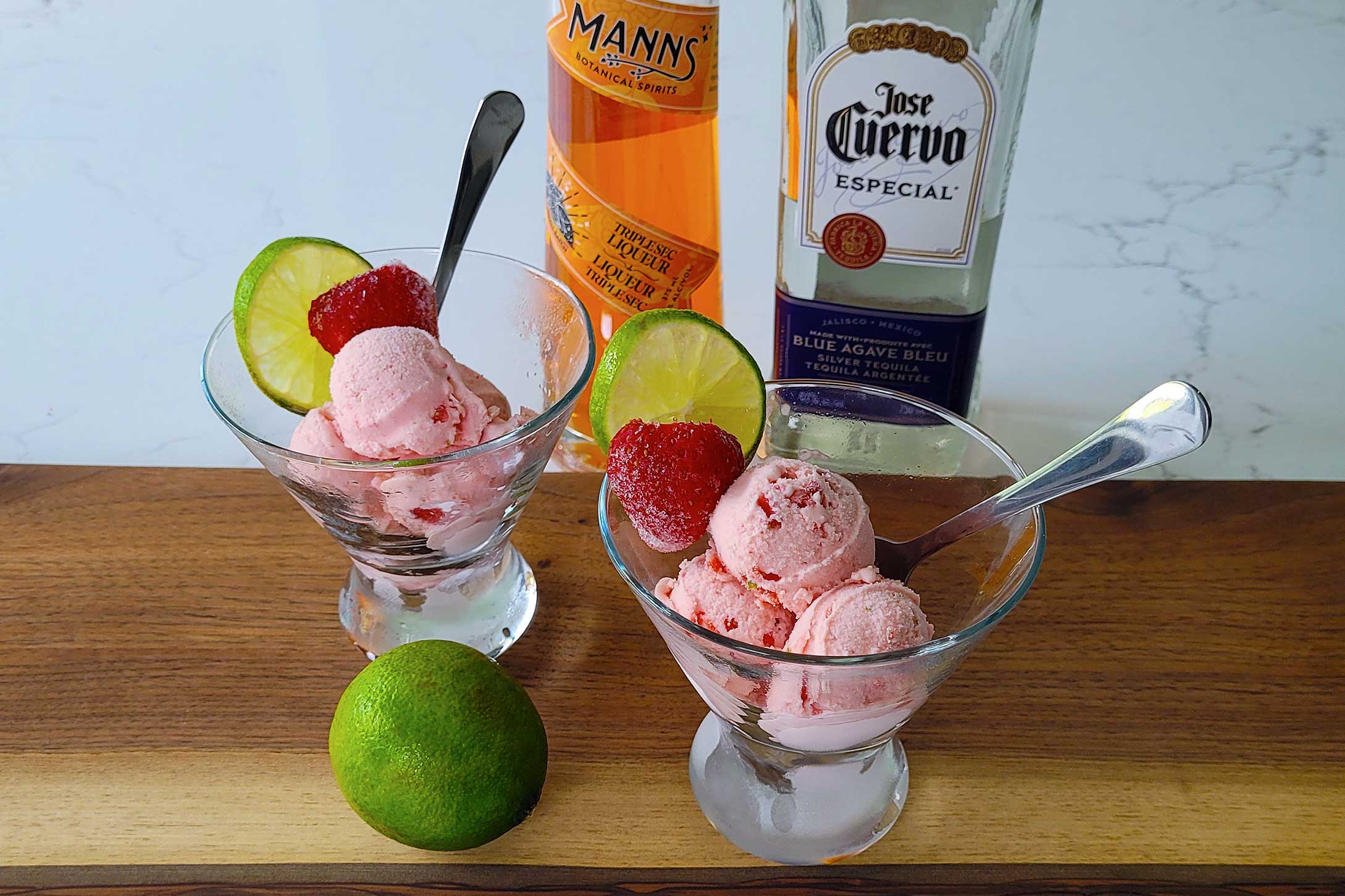 Two bowls of Strawberry Margarita Ice Cream with strawberries and lime.