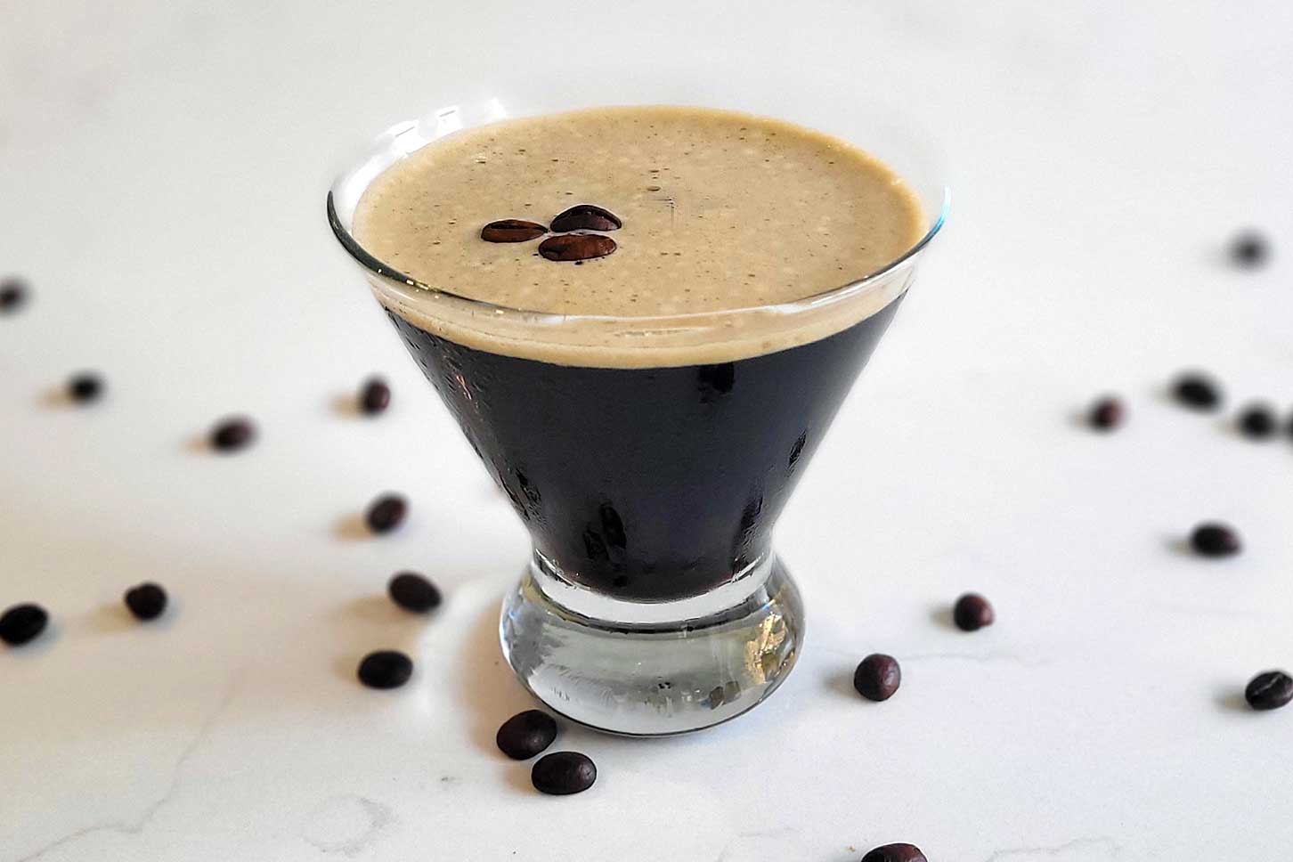 Espresso martini on a counter with espresso beans.