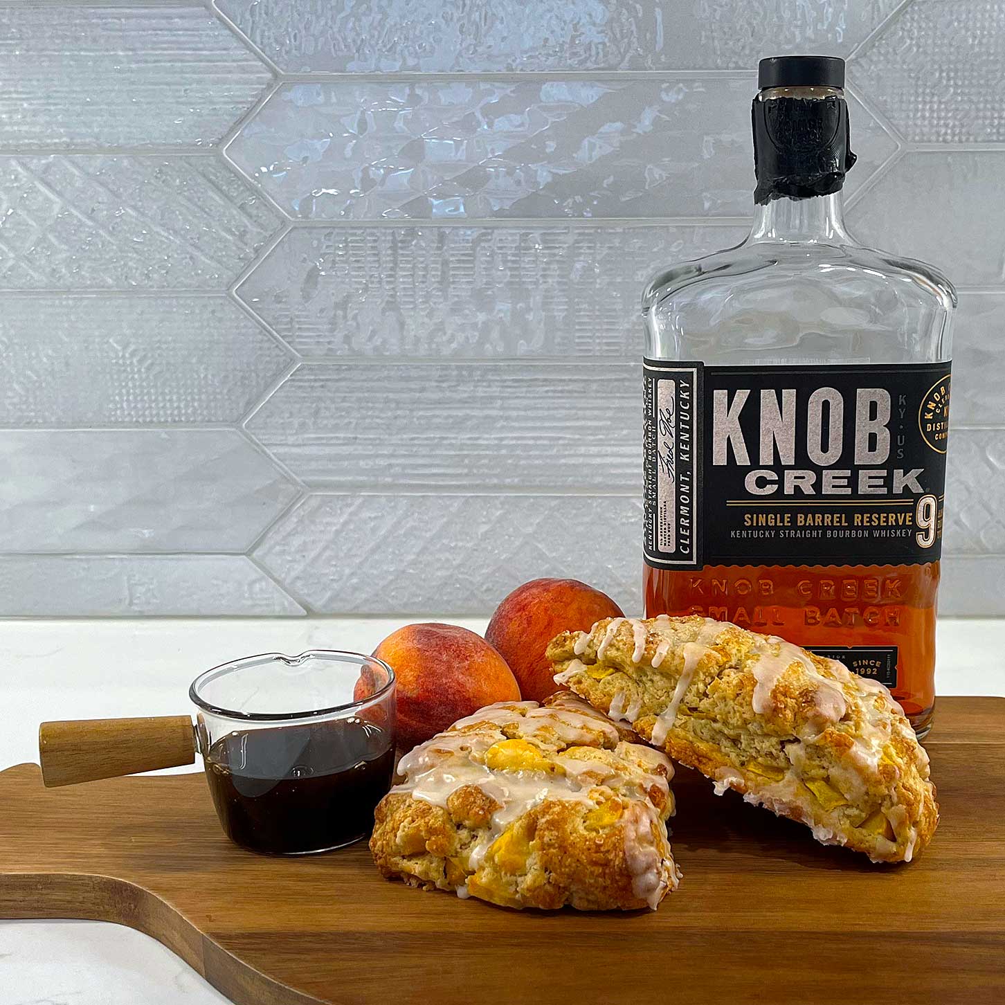 Vanilla peach scones with a bourbon glaze on a cutting board with peaches, vanilla, and a bottle of bourbon..
