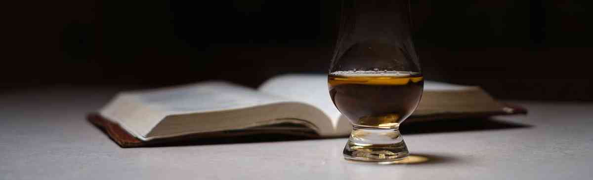 Glass of whisky and a book on a table.