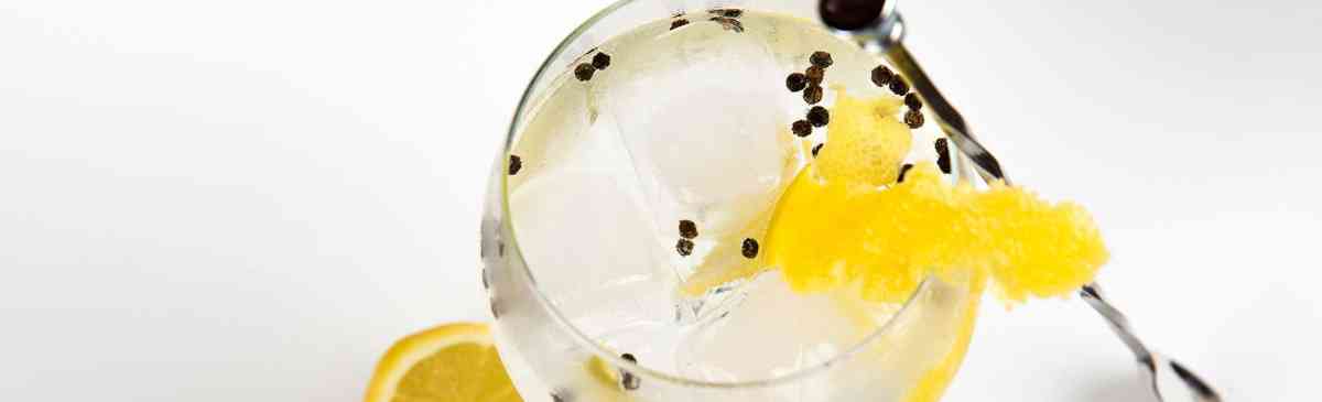 Glass filled with gin with peppercorns and lemon.