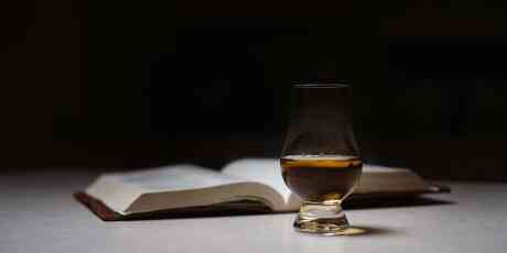Glass of whisky and a book on a table.