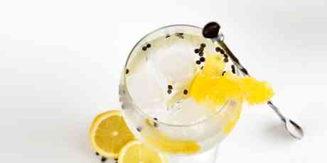 Glass filled with gin with peppercorns and lemon.