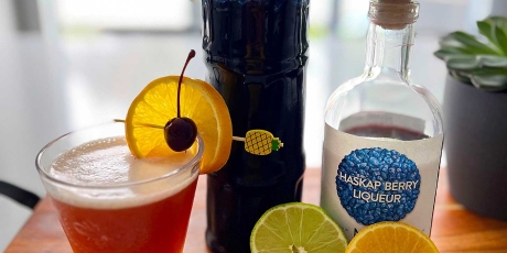 Haskap Berry cocktail on a counter with lemon, lime, and Haskap Berry liqueur. Haskap Sling on a counter with lemon, lime, and Haskap Berry liqueur.