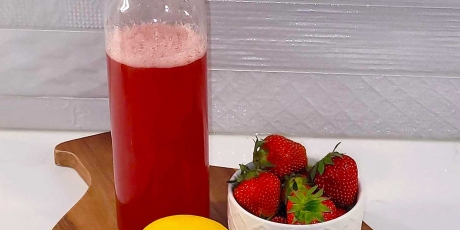 Strawberry simple syrup on a cutting board with a lemon and bowl of strawberries.