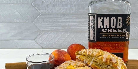 Vanilla peach scones with a bourbon glaze on a cutting board with peaches, vanilla, and a bottle of bourbon..