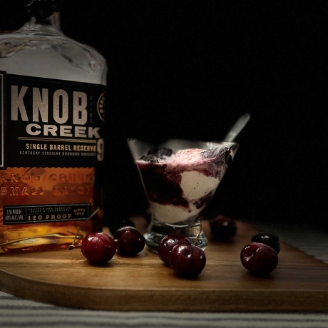 Smoked Bourbon Cherry Sauce over ice cream with a bottle of bourbon.