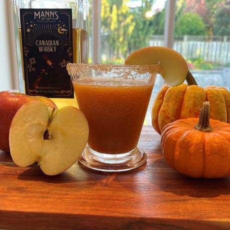 Cozy fall pumpkin cocktail on counter with a bottle of whisky, gourds, and apples.