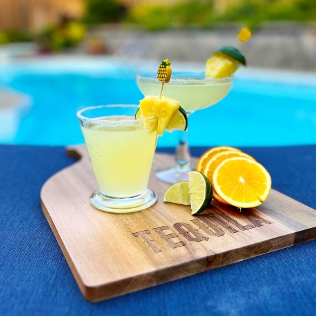 Pineapple Maragaritas on a cutting board by a pool.