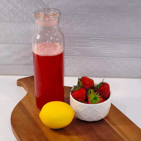 Strawberry simple syrup on a cutting board with a lemon and bowl of strawberries.