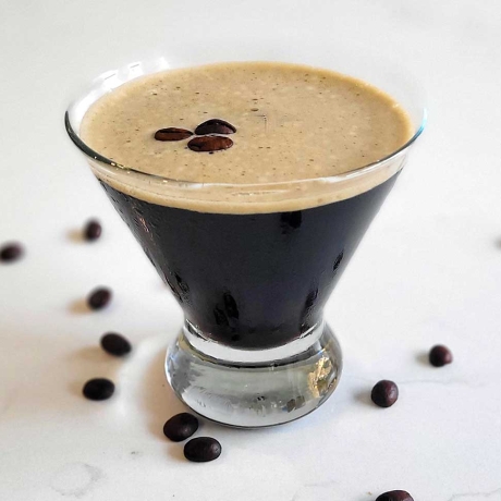 Espresso martini on a counter with espresso beans.