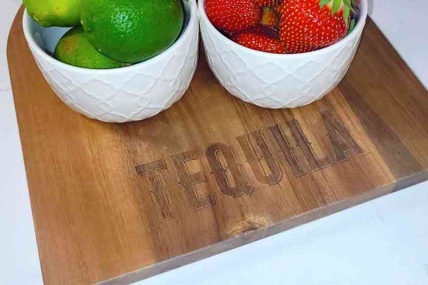 Tequila branded cutting board with bowls of strawberries and limes.