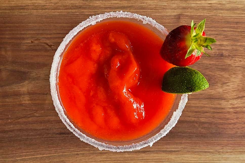 A frozen strawberry margarita with a lime wedge and fresh strawberry garnish.