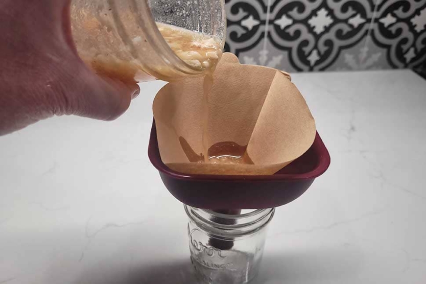 Straing bacon fat washed bourbon through a coffee filter to remove the fat solids.